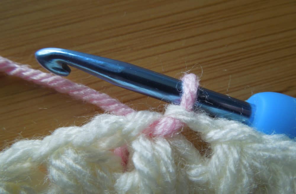 Insert hook into top of 1st puff stitch and pull up a loop of pink yarn