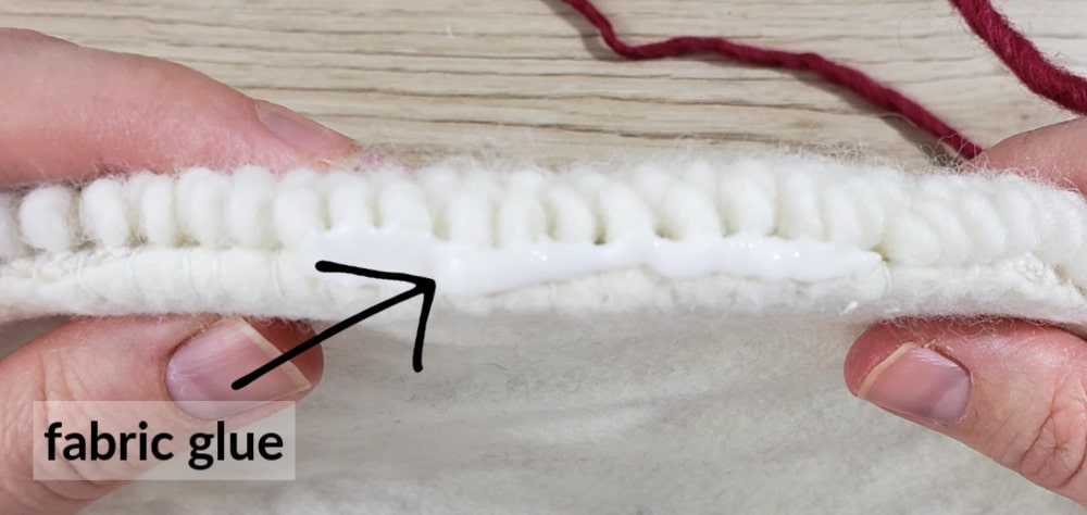 Putting fabric glue around edge of punch needle trivet for trim