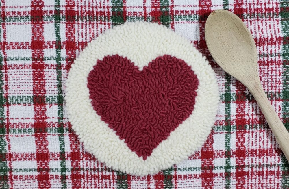 Heart Punch Needle Trivet with a cloth napkin and a wooden spoon
