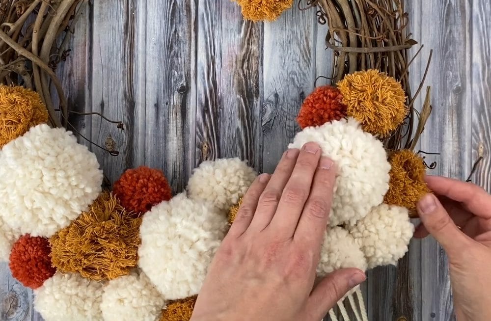 attaching the pom poms to the macrame fall wreath