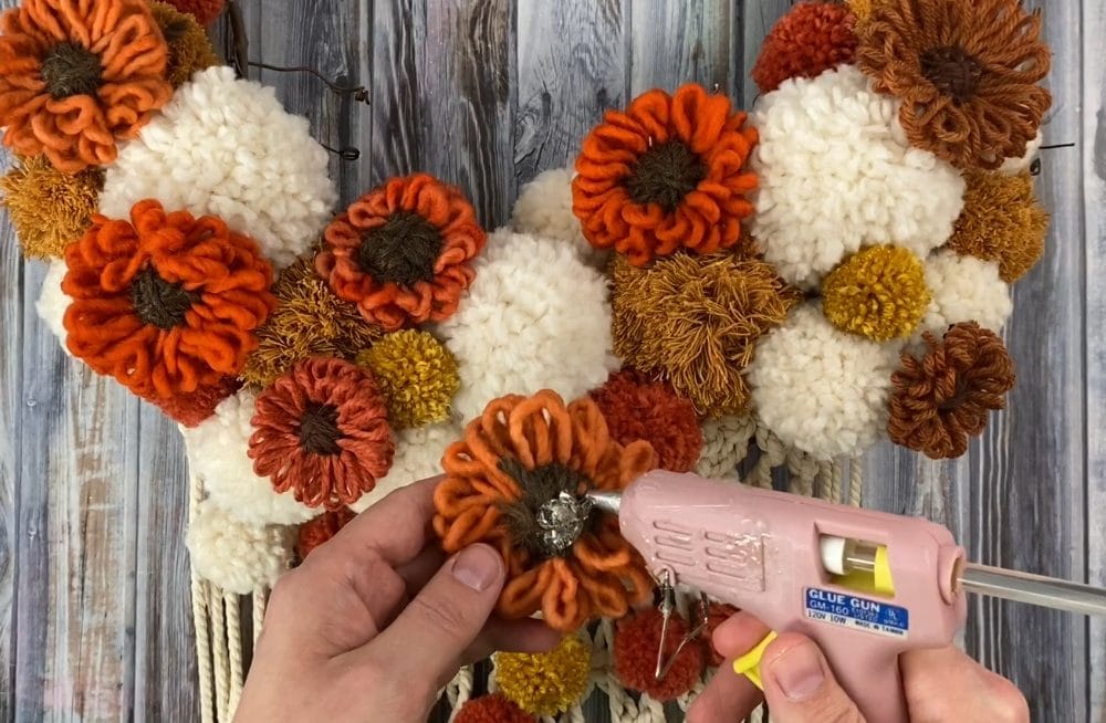 gluing down the yarn flowers on the macrame wreath