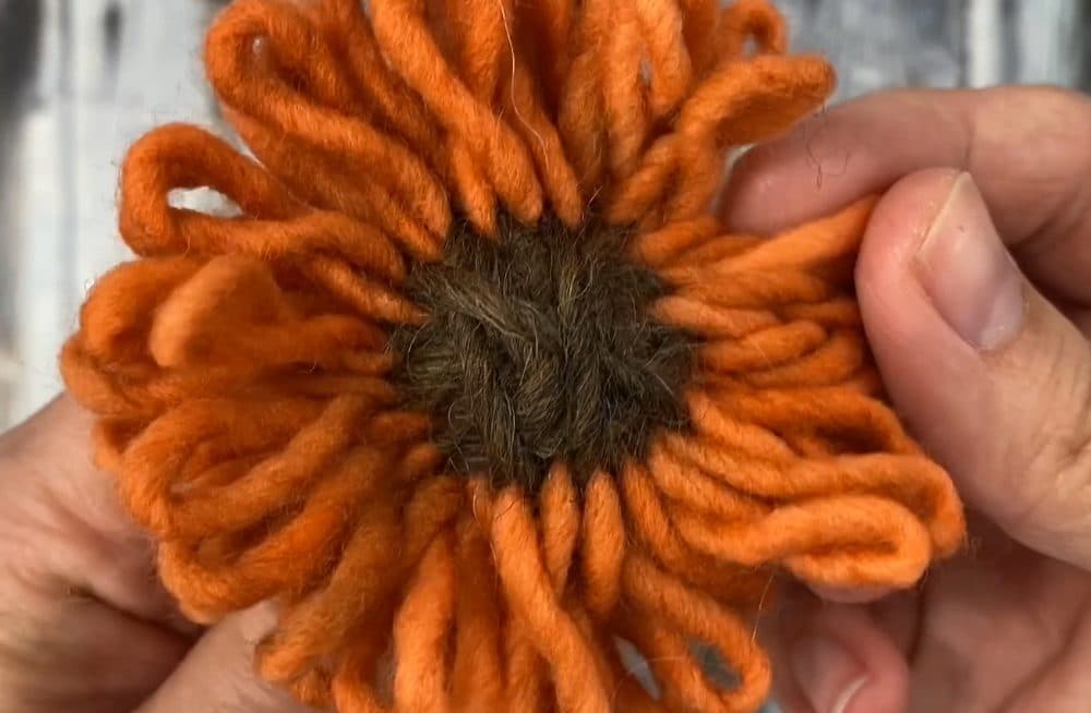 close up of orange and brown yarn flower made on flower loom