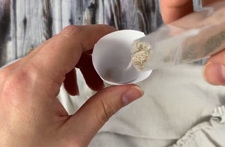 using a paper funnel to pour some glitter in the DIY glitter ornament