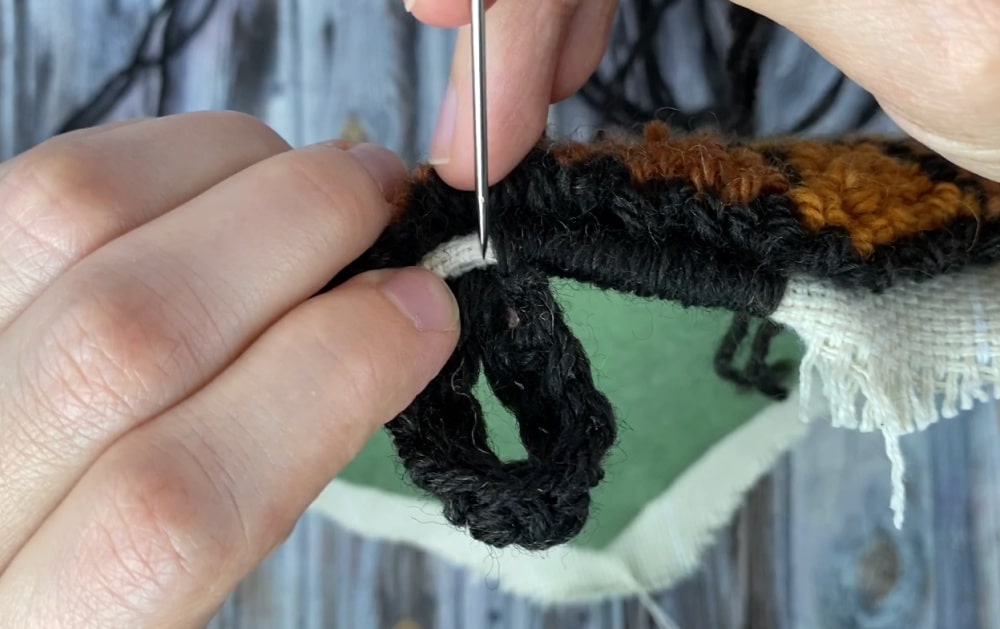 adding the hanging loop to the edge of the punch needle acorn trivet pattern