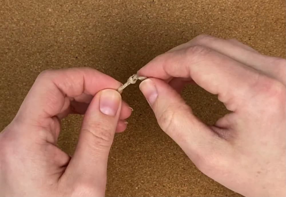 tying overhand knots in the ends of the cord of beaded macrame bracelet