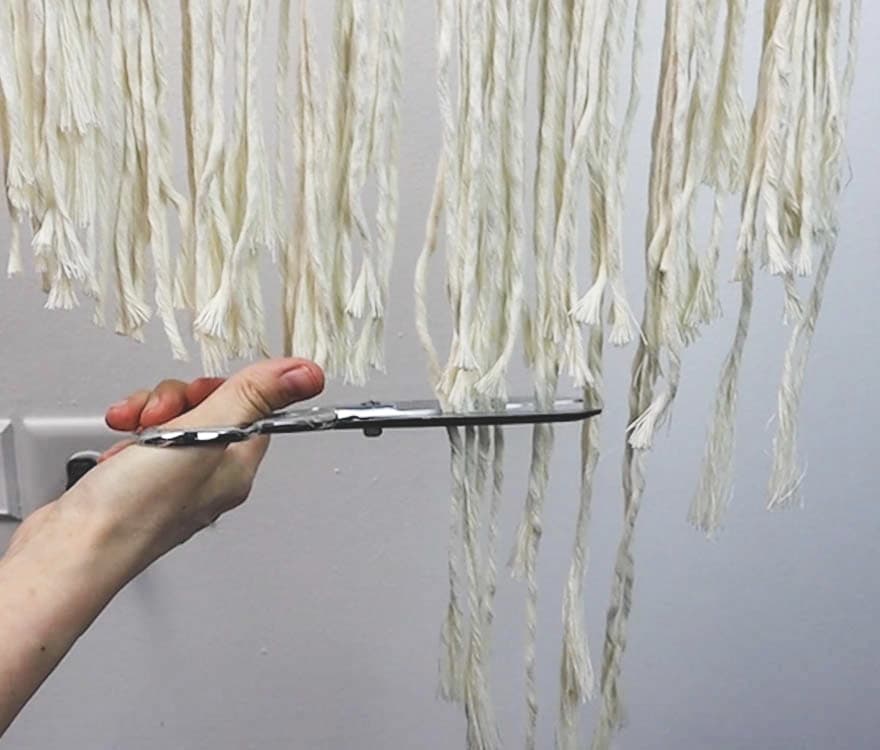 trimming the fringe at the bottom of macrame tree of life wall hanging