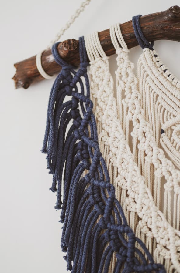 close up of a navy and white macrame wall hanging on a brown tree branch