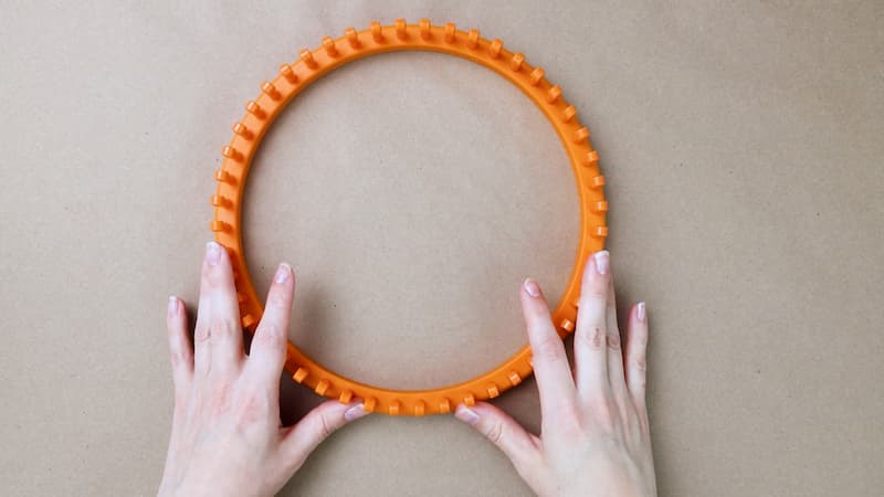 orange adult size hat loom and a woman's hands