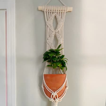 diamond macrame plant hanger wall hanging hung up on a light gray wall next to a white door