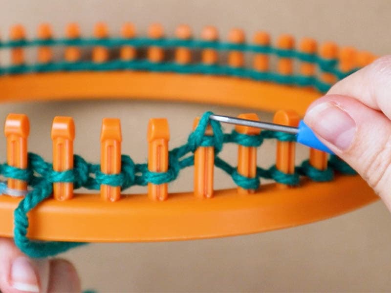 pulling the stitch over and off the peg of the knitting loom