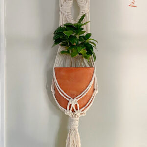 diamond macrame plant hanger wall hanging hung up on a light gray wall next to a white door