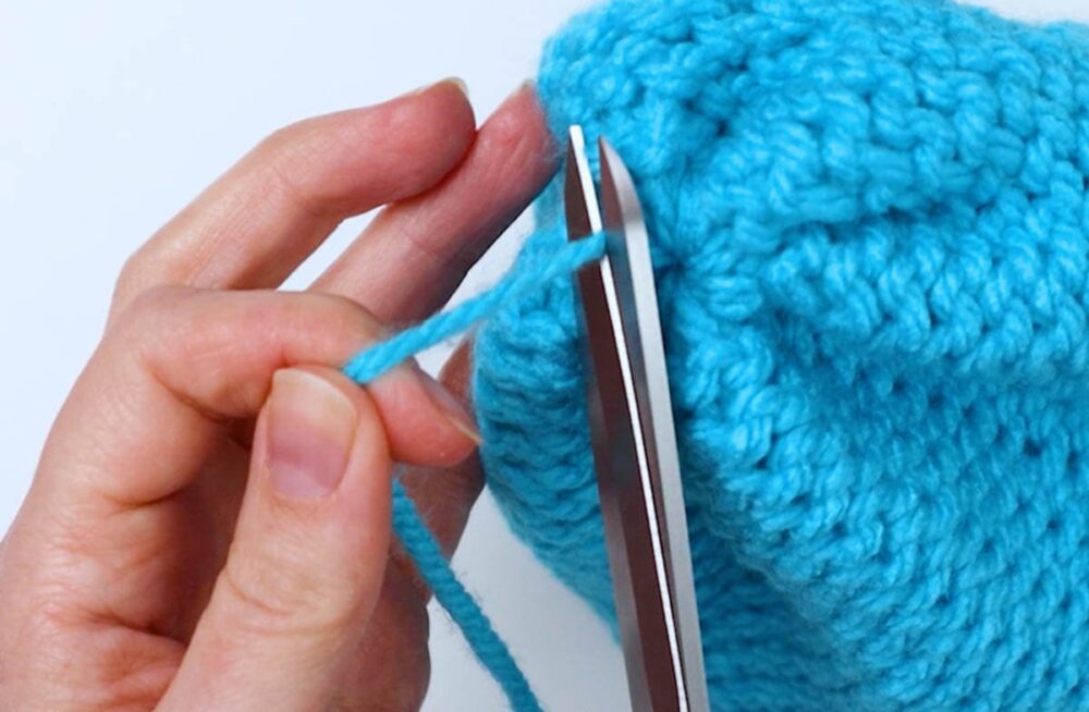 trim off the excess yarn from the top of the loom knit baby hat