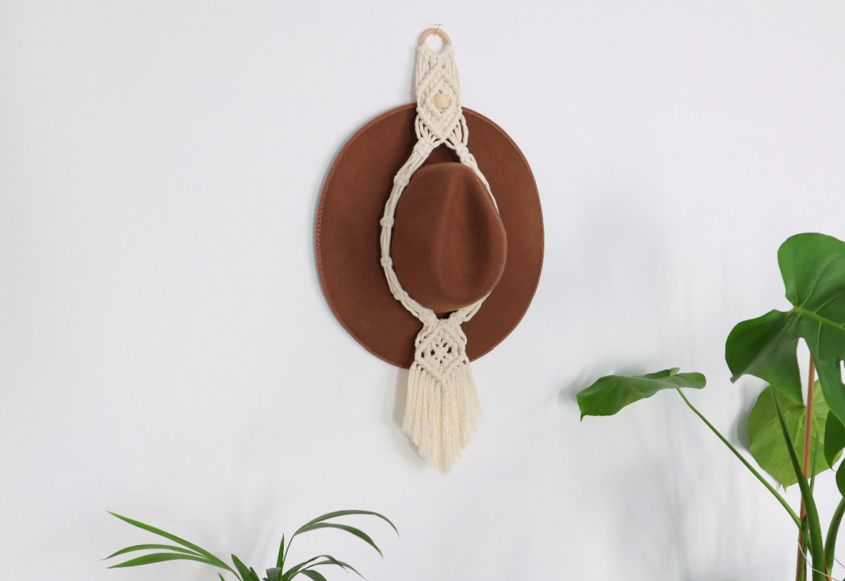 macrame hat hanger on the wall with a brown hat inside