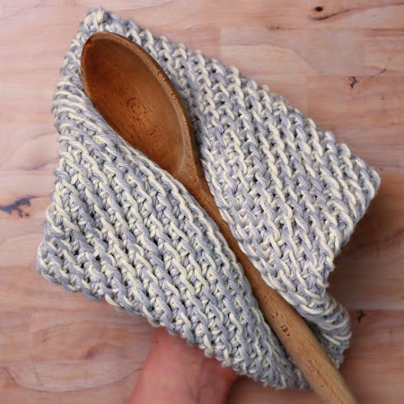 gray and white crochet pot holder with a wooden spoon