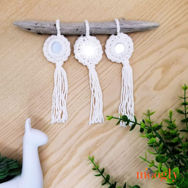 3 crochet mirror ornaments hanging from a piece of driftwood