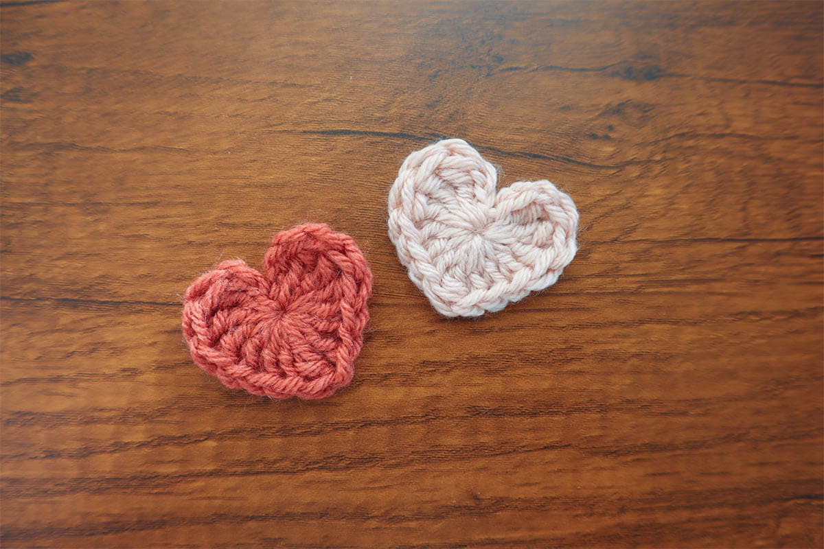 two of the small hearts in pink and red laying on a wooden desk